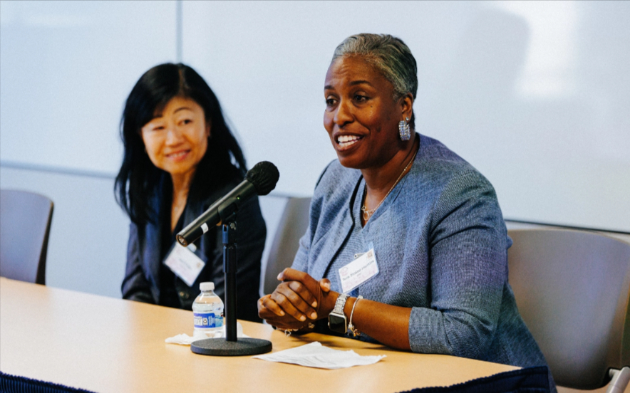 BART's Tera Stokes-Hankins speaking to the Girls in Motion Summit sitting at a desk behind a mic with another BART female engineer looking on.